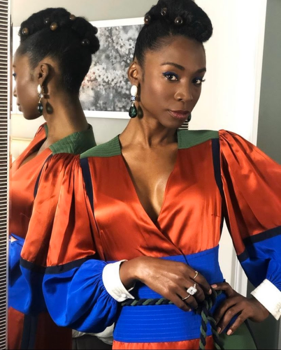 Angelica Ross in colorful silk blouse posed with a mirror to her back