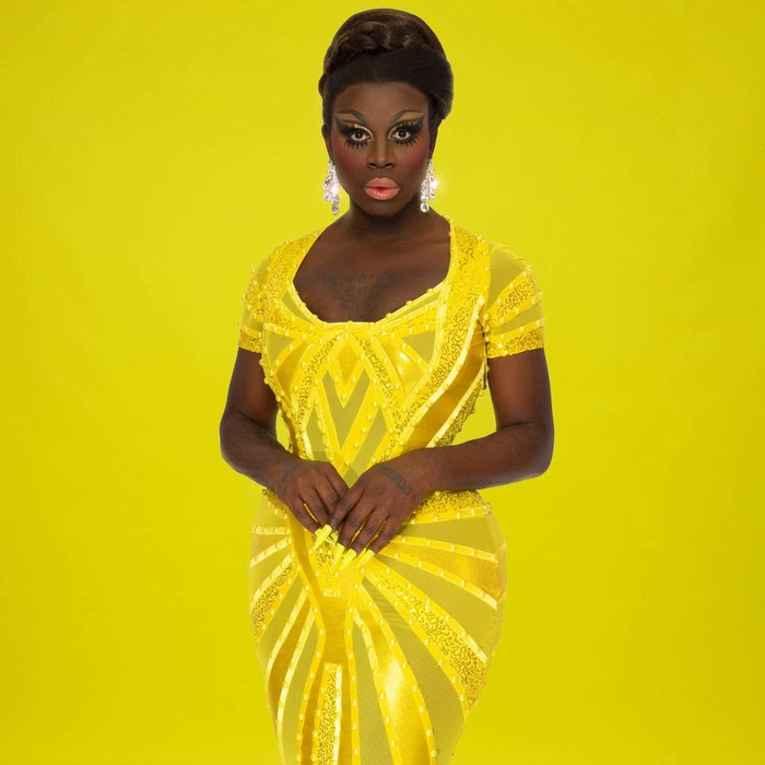 Bob the Drag Queen in a form-fitting yellow sequinned dress with geometric patterns, and crystal sparkly earrings