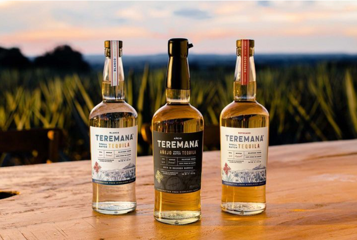 Teremana tequila, in a bottle that looks similar to wine, sitting on a wood table with a landscape of hills in the backdrop