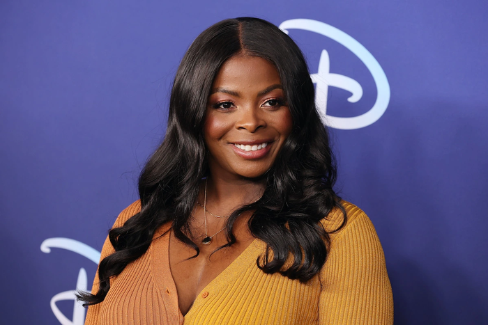 Janelle James in mustard yellow dress posing at an event for Disney