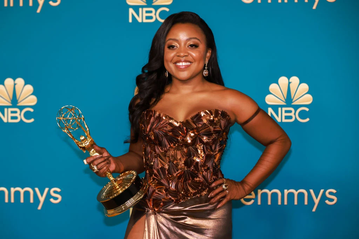 Quinta Brunson in golden sparkling dress holding an award at the Emmys