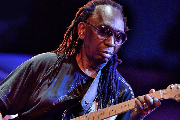 Thomas Mapfumo, in sunglasses and dreadlocks and black teeshirt playing guitar on stage