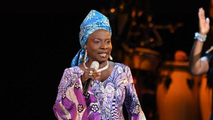 Angelique Kidjo in African patterned headwrap and dress, performing on stage