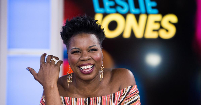 Leslie Jones, smiling. She is wearing a striped off-shoulder shirt and statement earrings