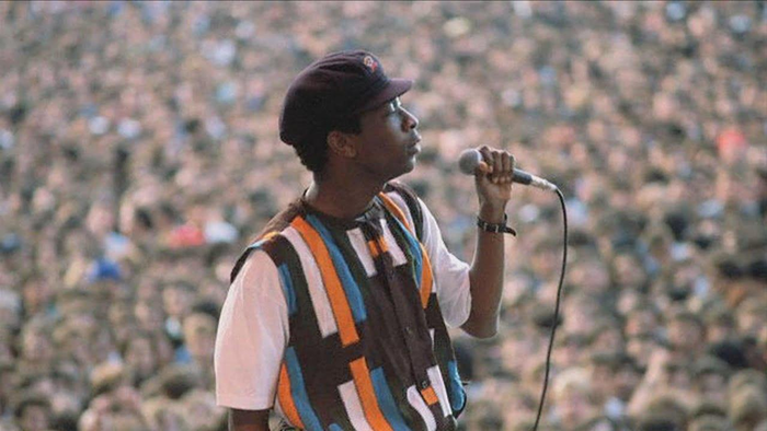 Youssou N'Dour in cap and colorful shirt singing in front of an audience