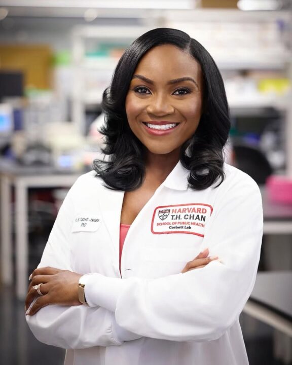 Dr. Kizzmekia Corbett, arms folded across chest and smiling proudly, at the Harvard laboratory