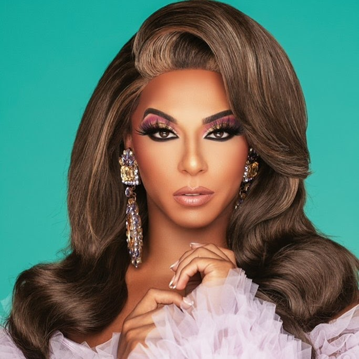 Shangela in tulle ruffle dress and huge sparkly statement earrings, with smooth brown wig and dramatic eyelashes