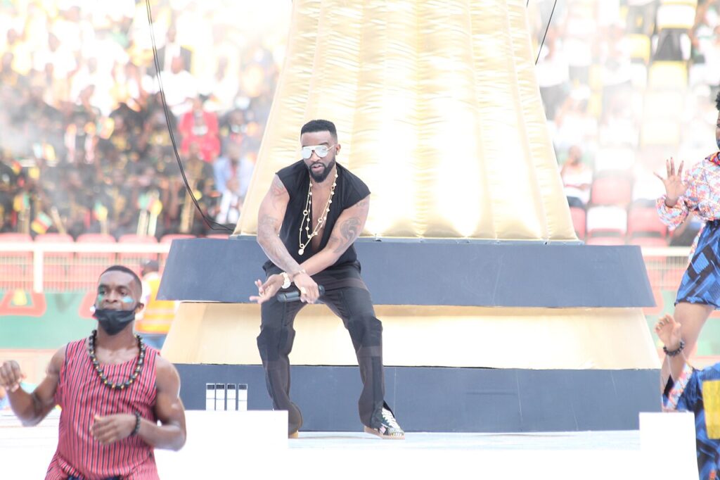 Fally Ipupa dancing on stage at concert/ He is wearing shutter shades and black shirt and pants