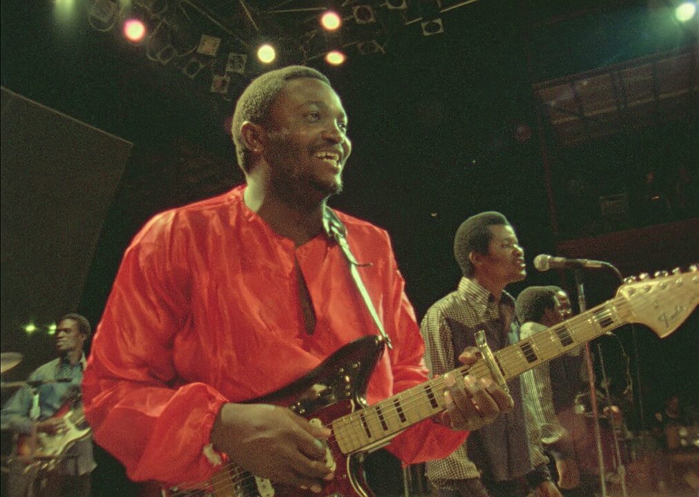 Franco Luambo in a red tunic on a guitar, and his band OK Jazz performing 