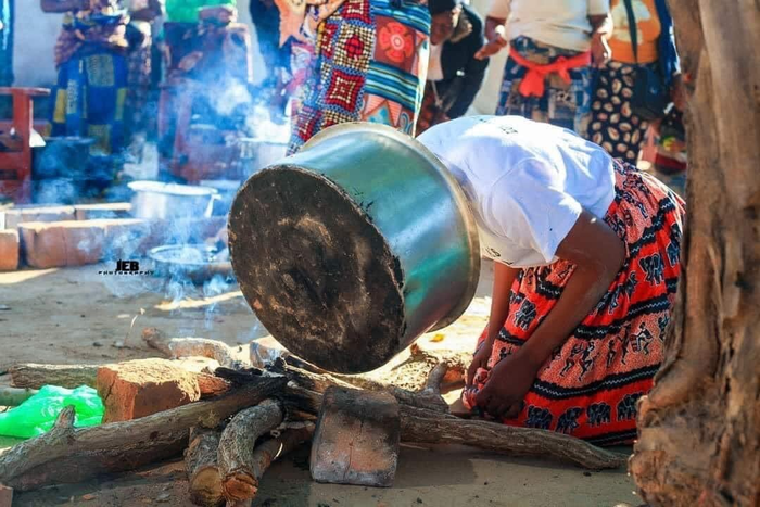 Bride with her head inside of pot while crouched down on the ground to cook