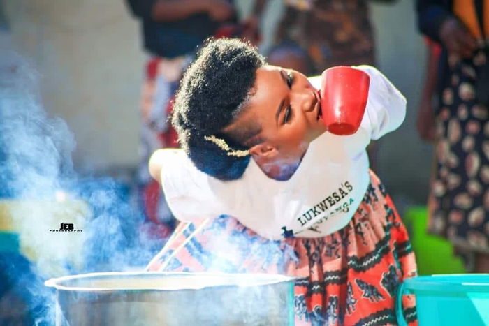 Bride holding cup with teeth with head tilted while her hands are behind her back. She is crouching over a steaming pot.