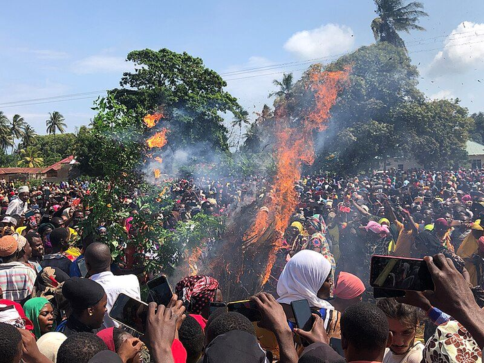 A crowd of people gather around the fire set to the ritual hut