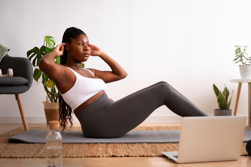 Black woman doing crunches while watching laptop in her living room