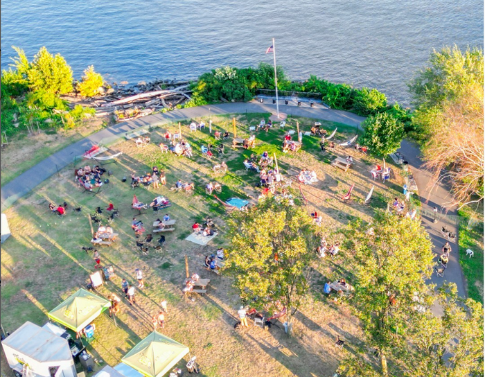 aerial view of a park facing the river with food vendor trucks and tents and people picnicking