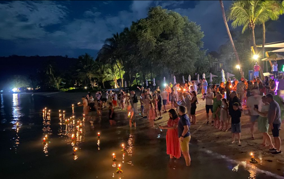 Tourists and locals in Phuket sending floating lights on the beach at nighttime.