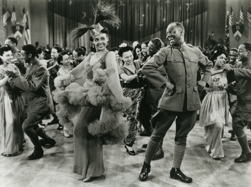 Bill Robinson in an army uniform, and Lena Horne in a feathered hat and tulle jacket with ruffles, and an evening dress, performing a dance