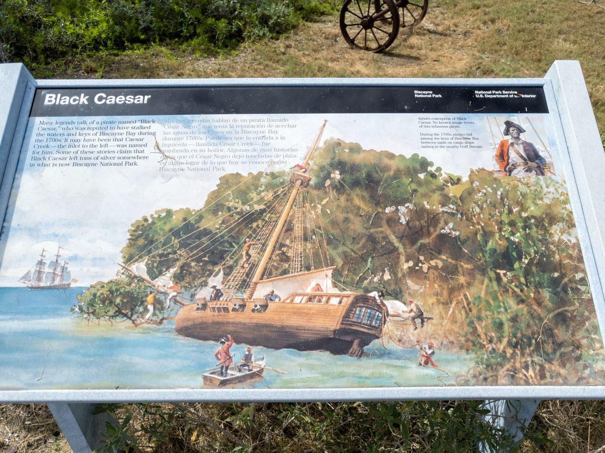 A sign at a park describing Black Caesar, with an illustration of his ship and crew on an island