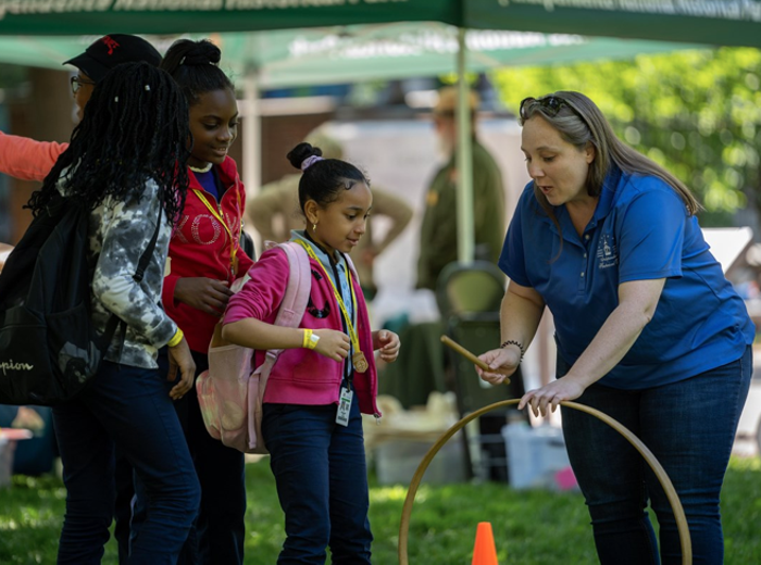 An African American family being shown by guide how to play the colonial hoop and stick game