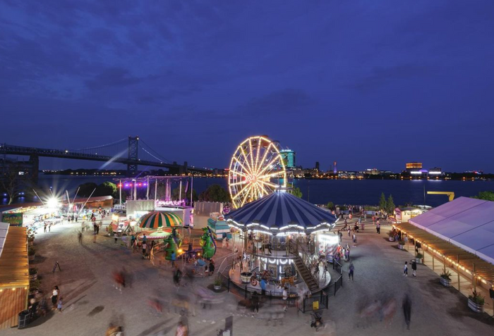 view of boardwalk at nighttime with a carousel, ferris wheel, and food stands. a bridge over the river is also in the view