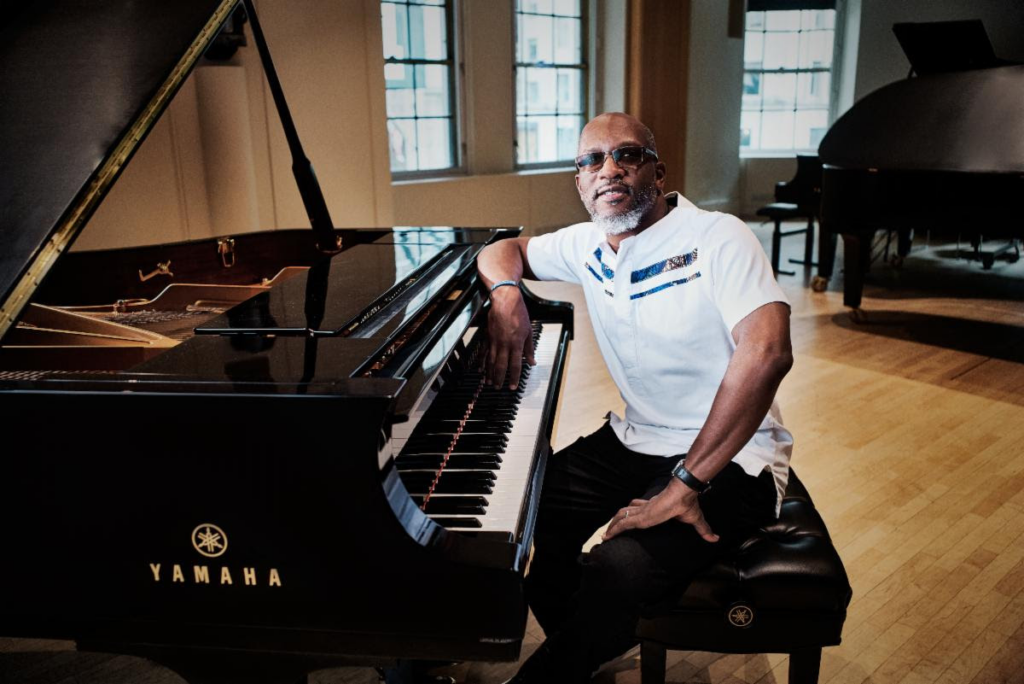 Pianist Orrin Evans seated and leaning against a Yamaha piano at  concert hall