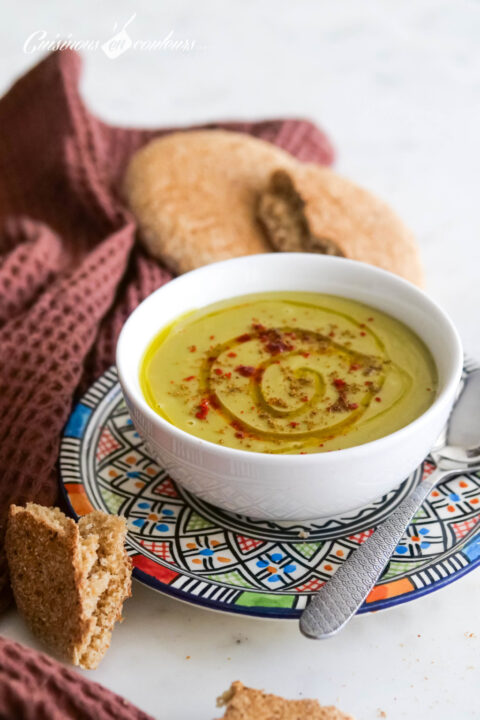 A tan green colored soup with a swirl of olive oil and ground red pepper powder on top