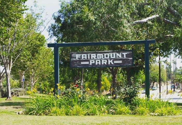 a wooden sign for Fairmount Park in front of a playground and greenery