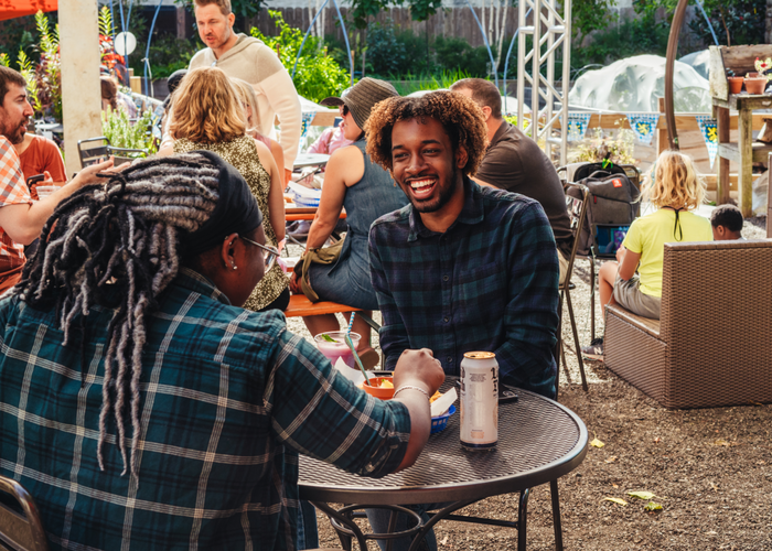 An African-American man and woman enjoying a meal, sitting in a garden-like setting with other people enjoying food and drinks in the background