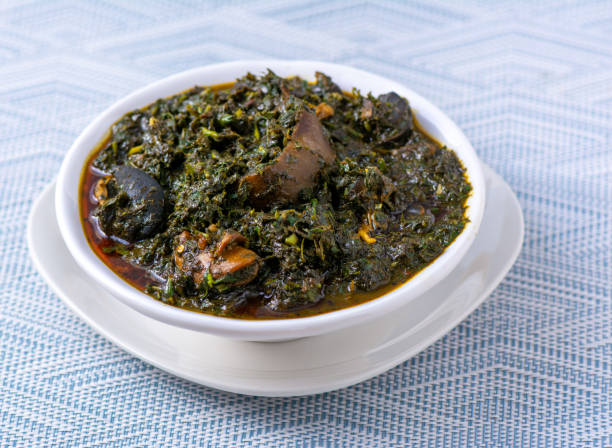 A dark brown soup full of greens and meat