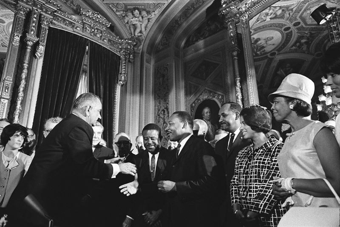 Black and white photograph of President Lyndon B. Johnson and Martin Luther King, Jr. at the SIgning of the Voting Rights Act of 1965. Other government leaders are also in attendance.