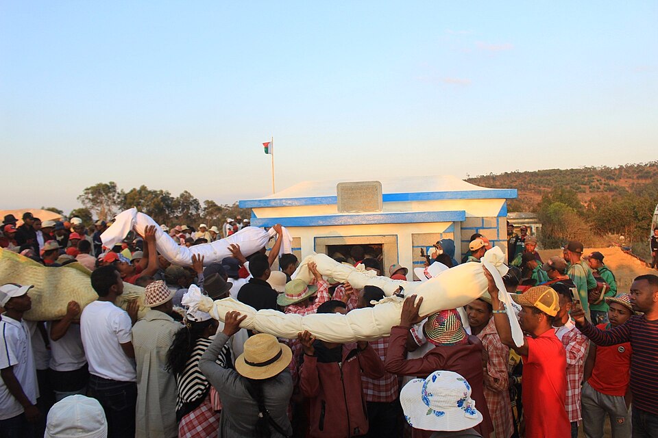 a packed crowd of locals carrying remains of the dead wrapped in sheets above their heads in celebration