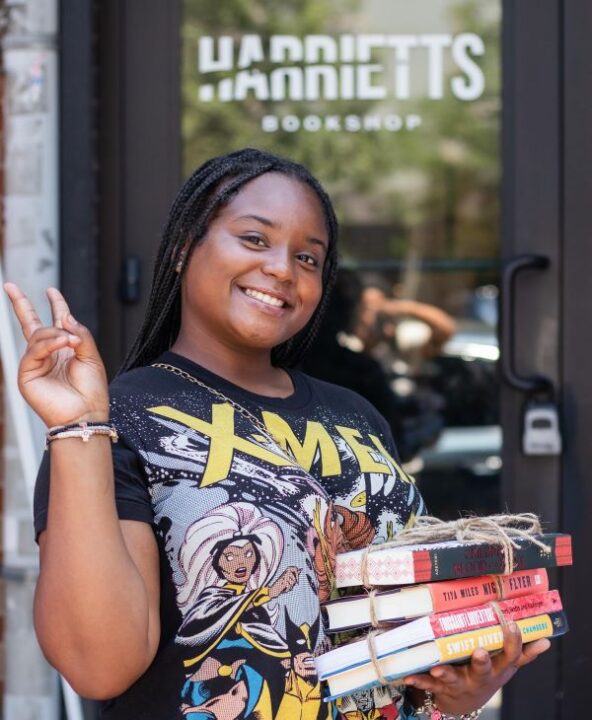 African American woman holding books tied up with string and posing with a smile and peace sign