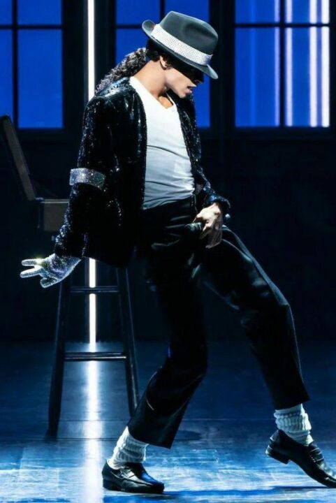 Michael Jackson in fedora, white shirt, sparkly jacket, and black pants, loafers, socks and his single glove on right hand.