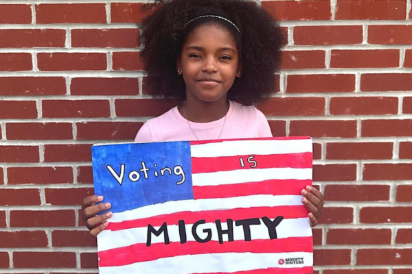 Young African American girl holding a handmade sign that looks like the American flag that says "Vote Mighty"