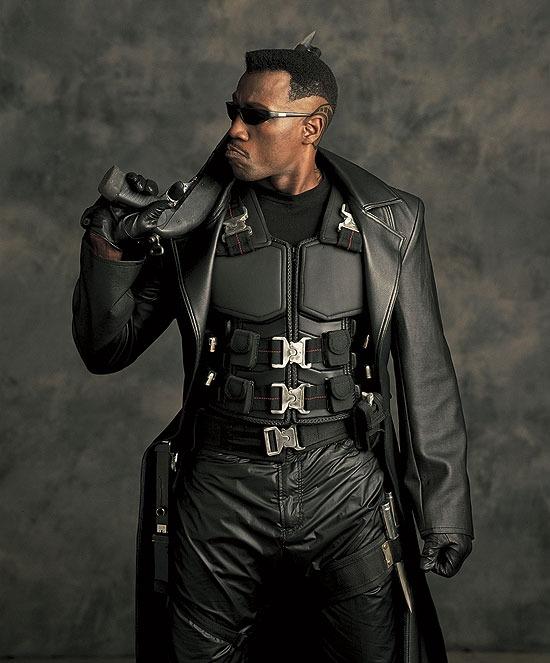 Wesley Snipes as Blade, wearing sunglasses, carrying a gun, leather jacket, body armor with buckles and embellishments, and leather pants also with weapon holsters.