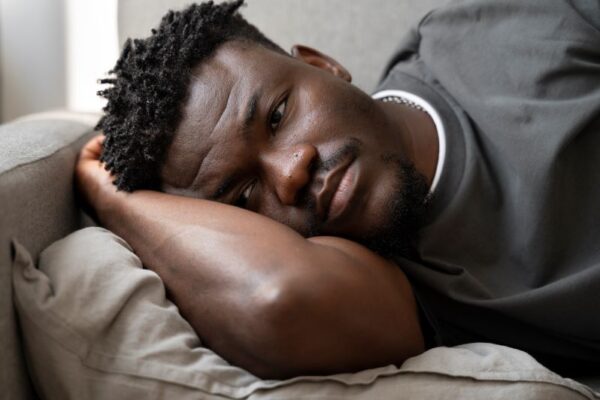 Depressed young African American man laying on bed