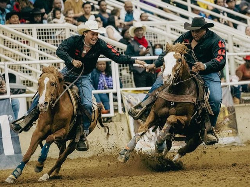 Two Black cowboys on horseback - one is passing a baton to the other