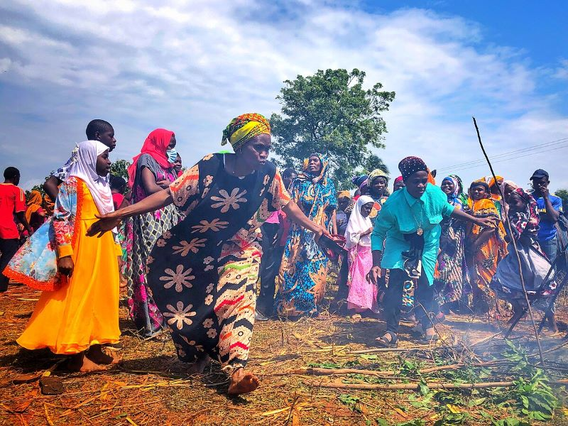 Women in colorful traditional attire standing around area with fire smoke