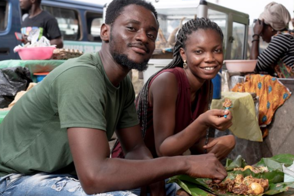 Young African man and woman seated and eating street food outdoors