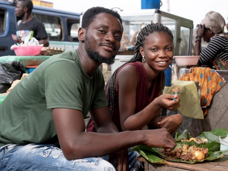 Young African man and woman seated and eating street food outdoors