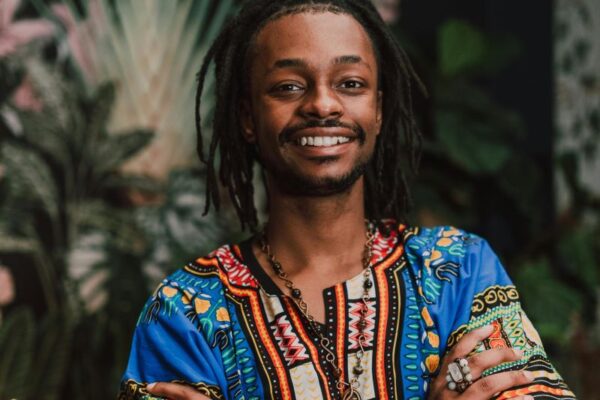 Young Black man in dreadlocks sporting a dashiki with arms folded across chest and friendly confident smile