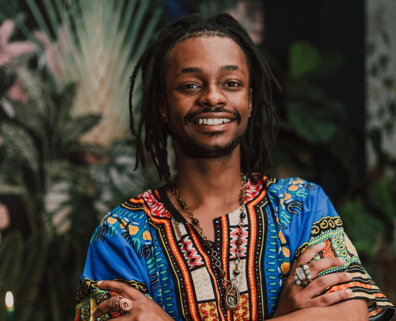 Young Black man in dreadlocks sporting a dashiki with arms folded across chest and friendly confident smile