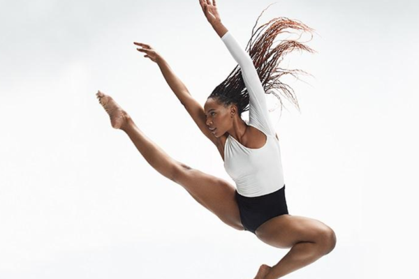 Black female dancer leaping dynamically, toes pointed, arms raised