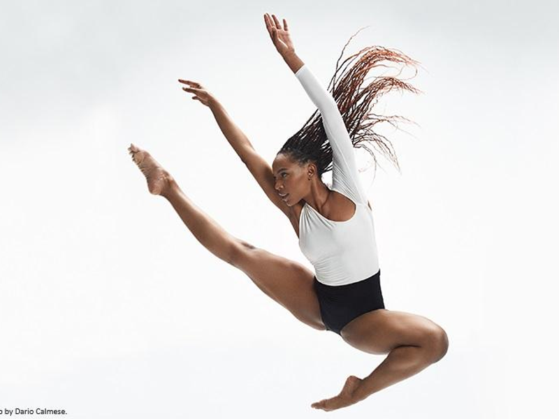 Black female dancer leaping dynamically, toes pointed, arms raised