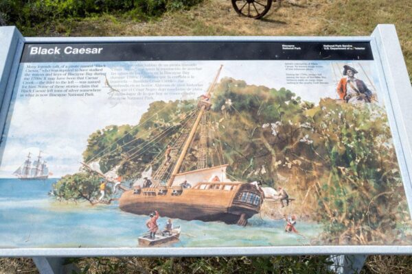 A sign at a park describing Black Caesar, with an illustration of his ship and crew on an island