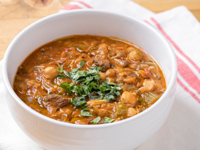 A rich brown soup full of vegetables, chickpeas, and meat