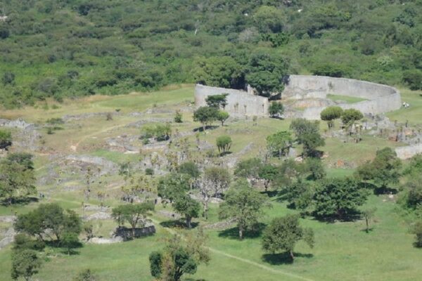 An aerial view of Great Zimbabwe with ruins of stone walls and structures in a field of green and trees