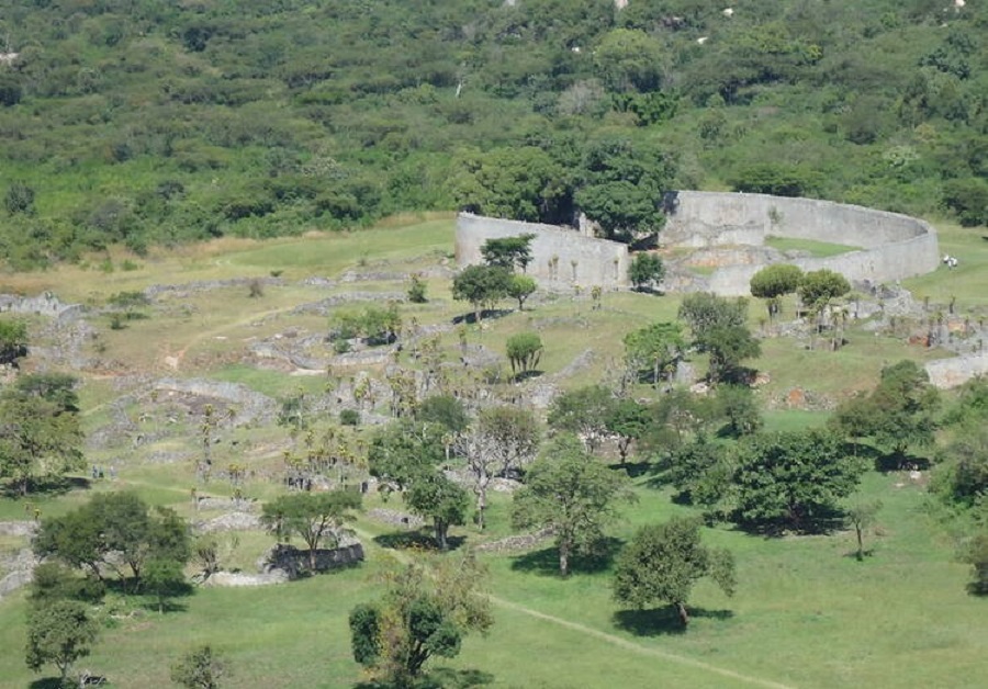 An aerial view of Great Zimbabwe with ruins of stone walls and structures in a field of green and trees