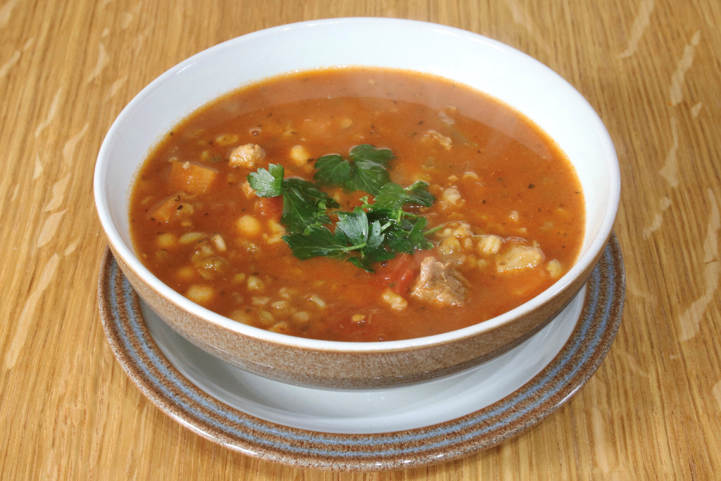 A brown soup with round grains (frik), meats, and topped with cilantro