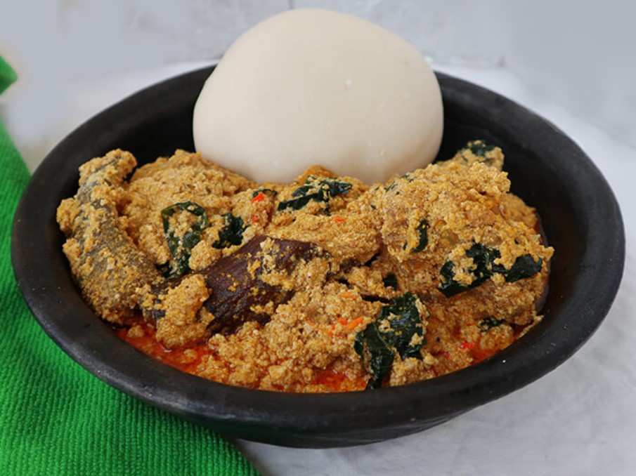 Egusi soup, in a broth with greens and meat, topped with a round ball of fufu