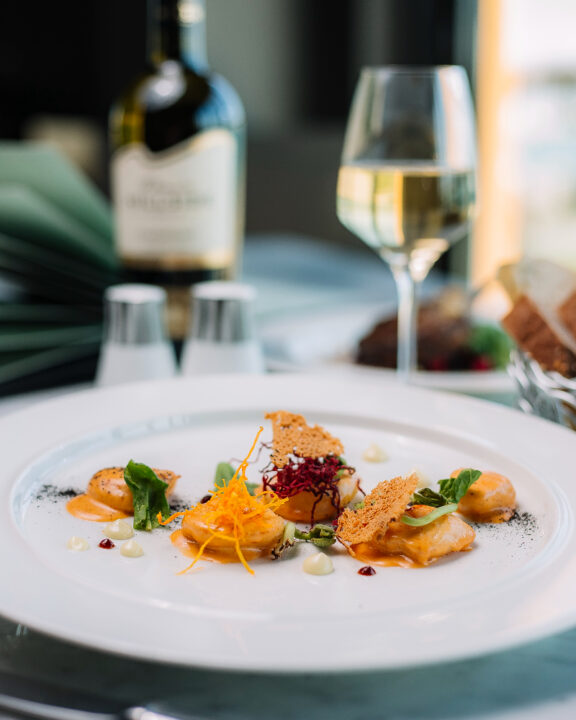 a shrimp appetizer with parmesan cheese crisp and herb garnish, there is a bottle of white wine and a long stemmed glass in the background.